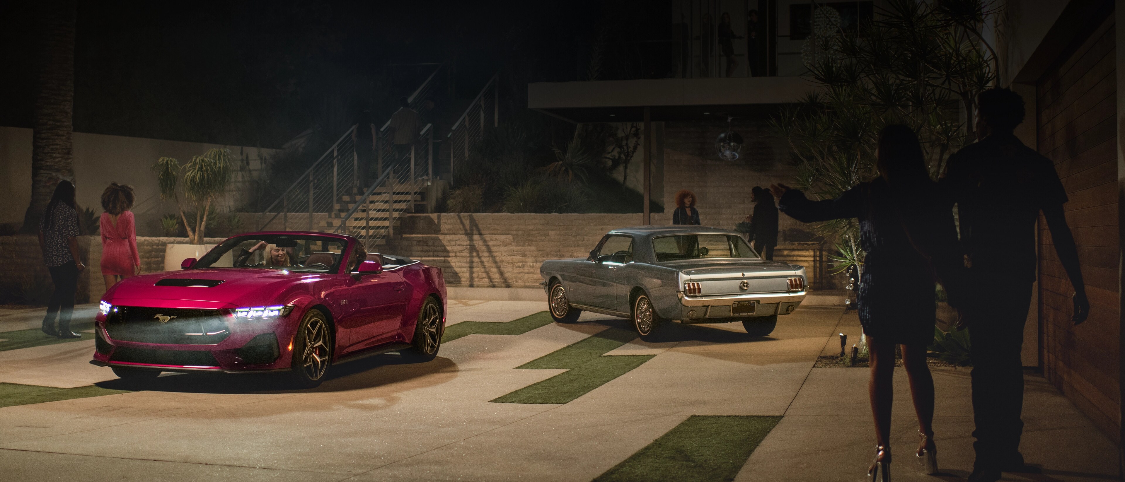 2025 Ford Mustang® GT convertible and a first-gen Mustang coupe parked in a driveway with people nearby