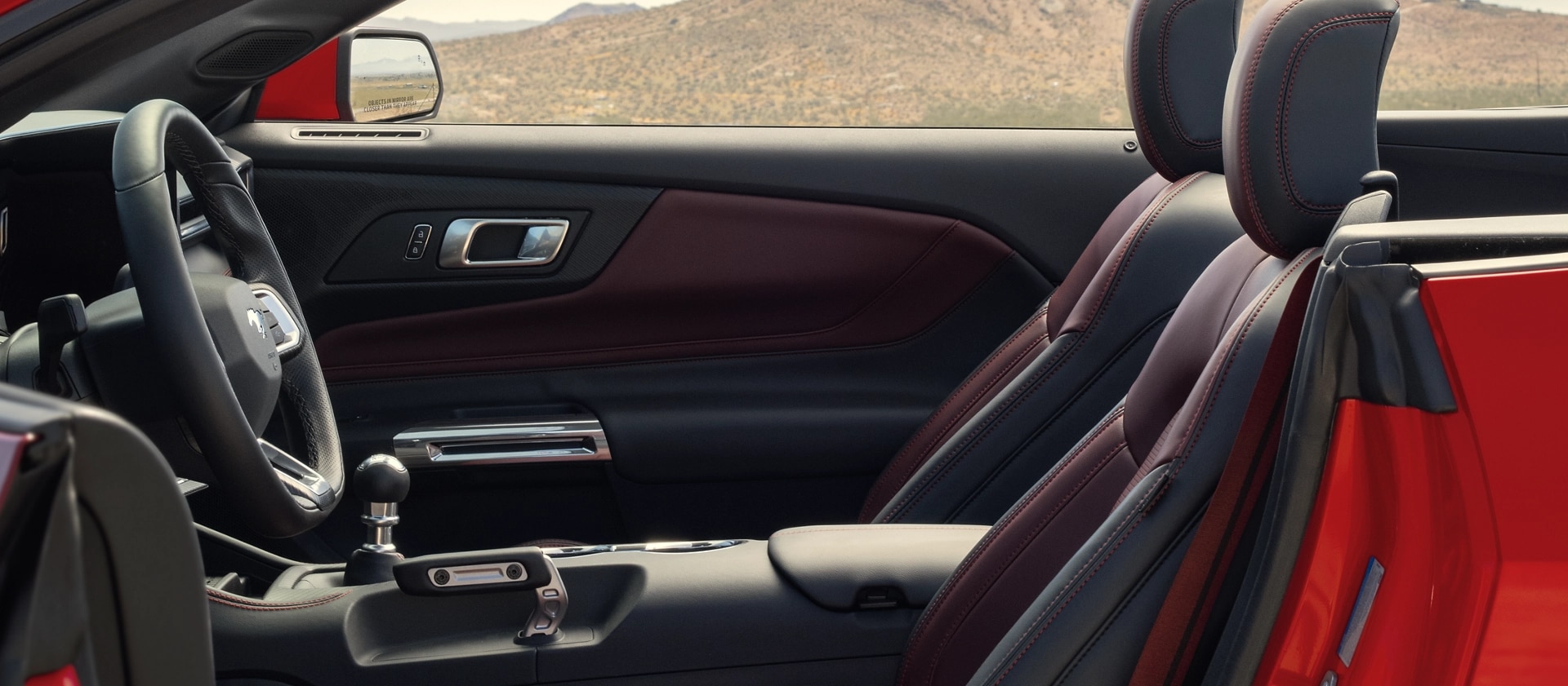 Parked 2025 Ford Mustang® convertible with the driver's side door open showing the available Carmine Red interior