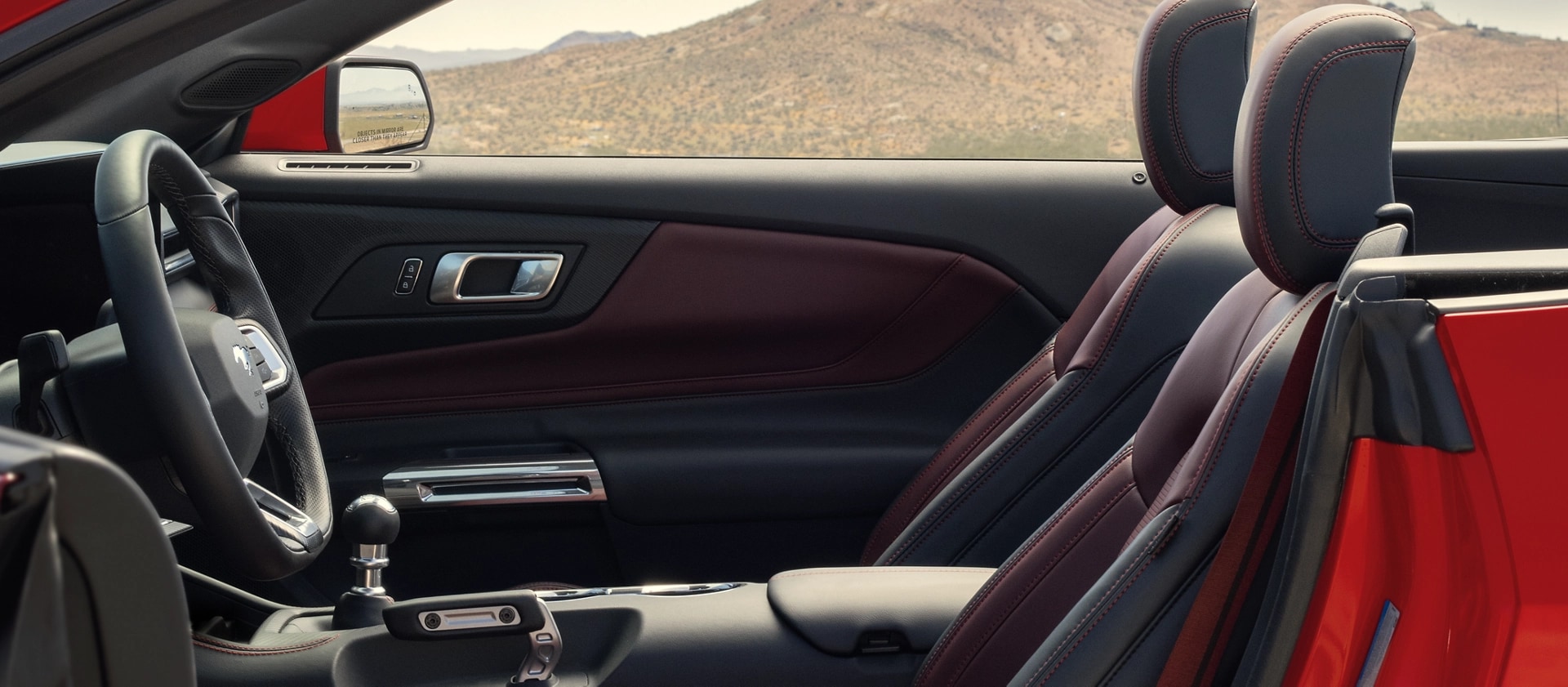 Parked 2026 Ford Mustang® convertible with the driver's side door open showing the available Carmine Red interior