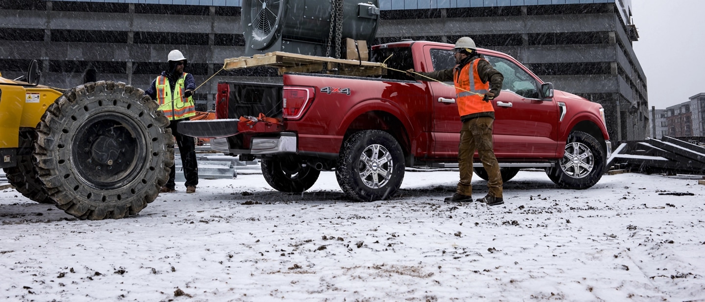 Two men load heavy equipment into the truck bed of an F-150.