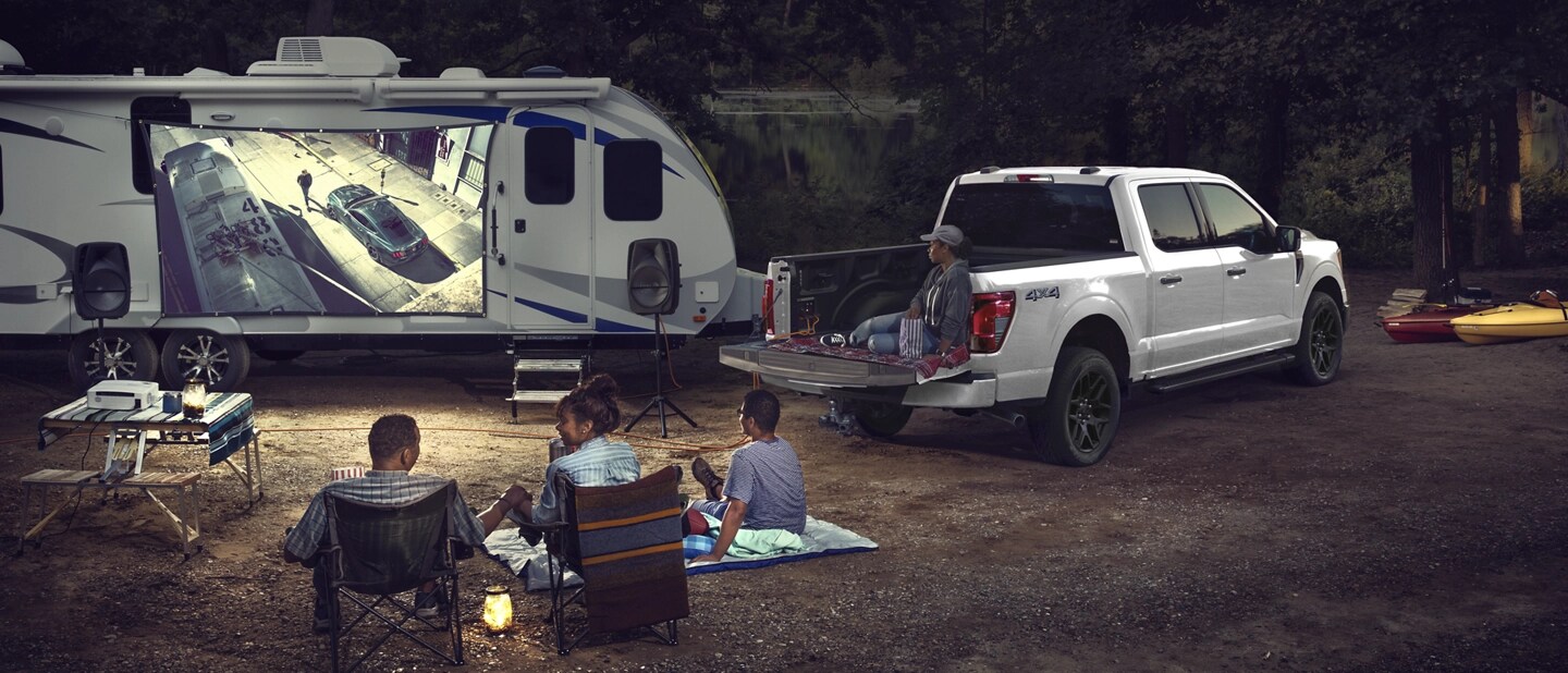 A family at a campsite watching a football match projected onto a trailer parked next to an F-150.
