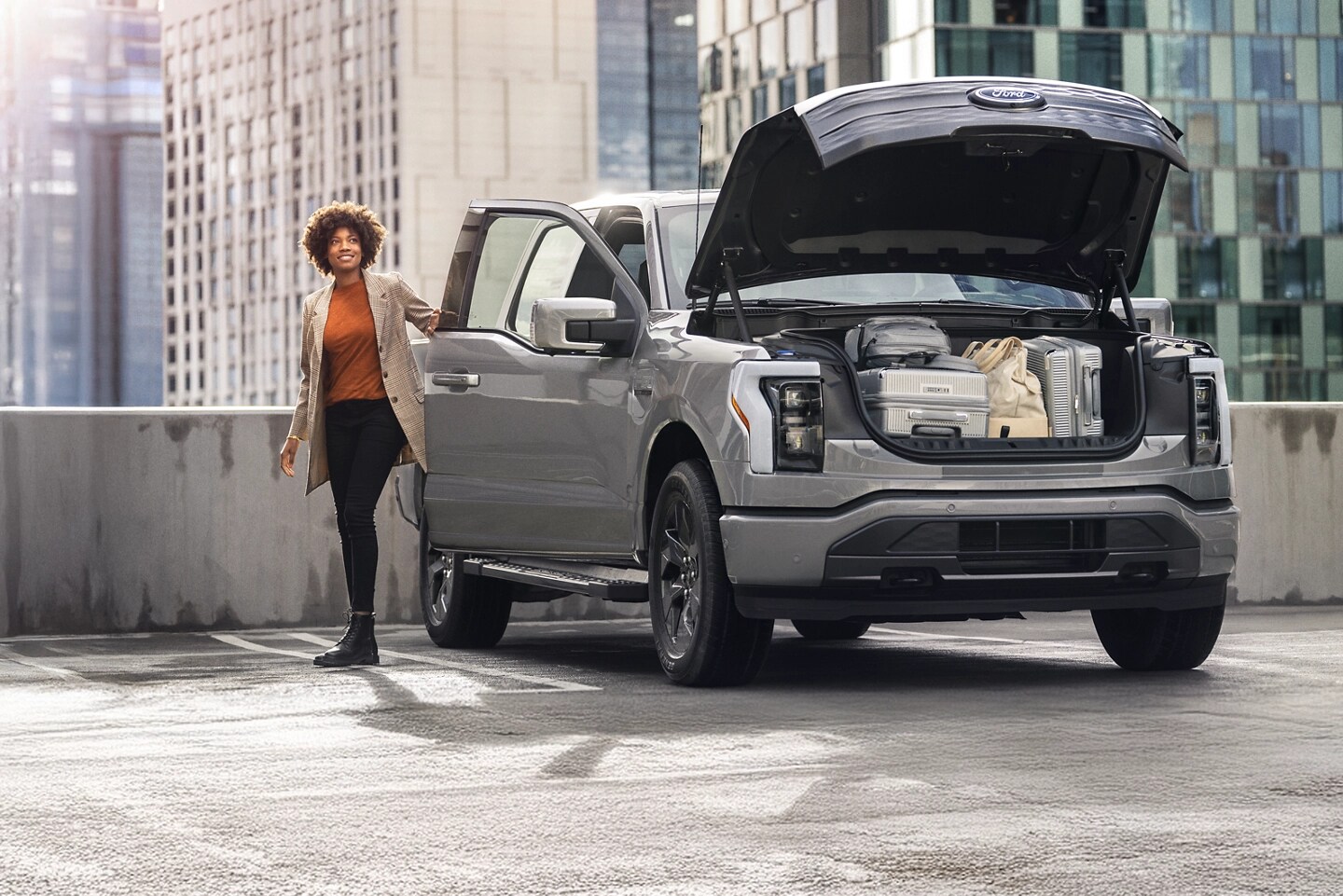 A woman stands next to an F-150 Lightning with an open frunk packed with luggage.