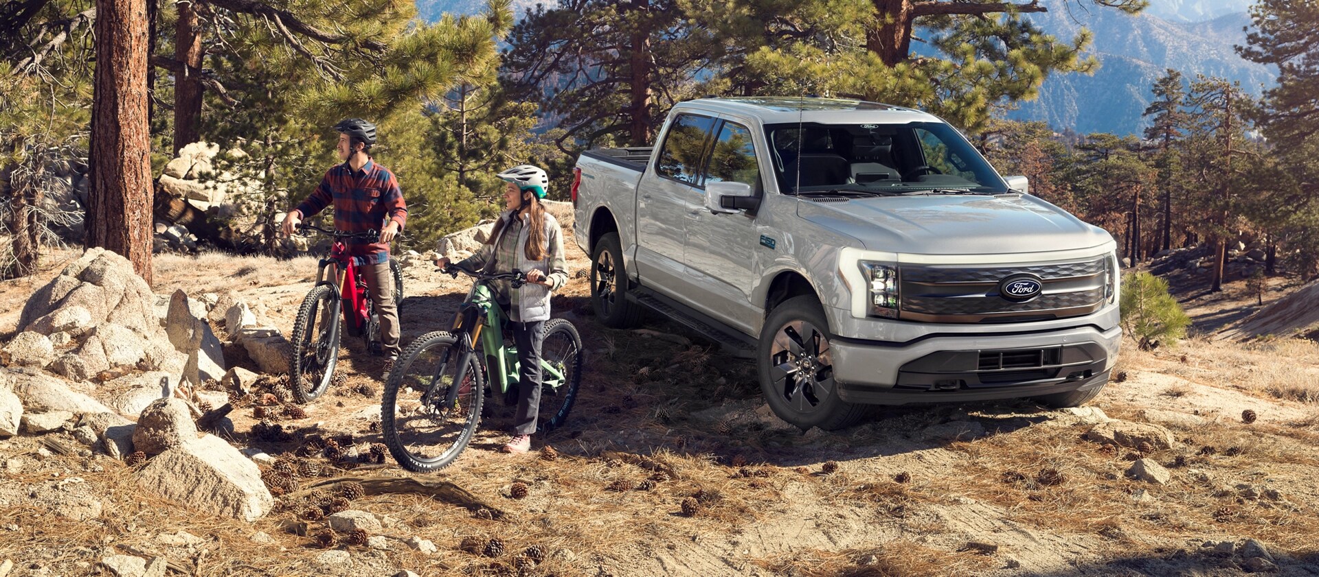 Two people on mountain bikes beside an F-150 Lightning parked on a rugged hill.