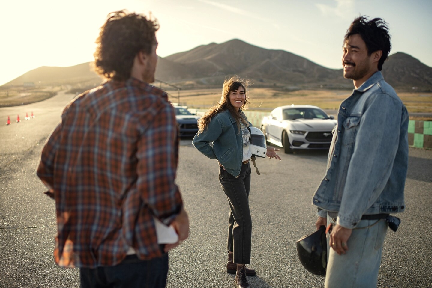 People gathered at a racetrack with Mustang vehicles in the background.