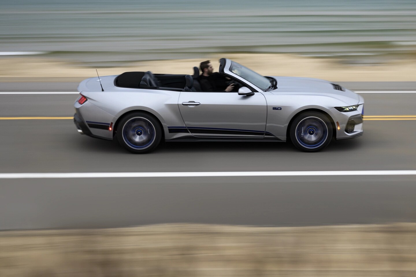 Mustang convertible driving on a highway.