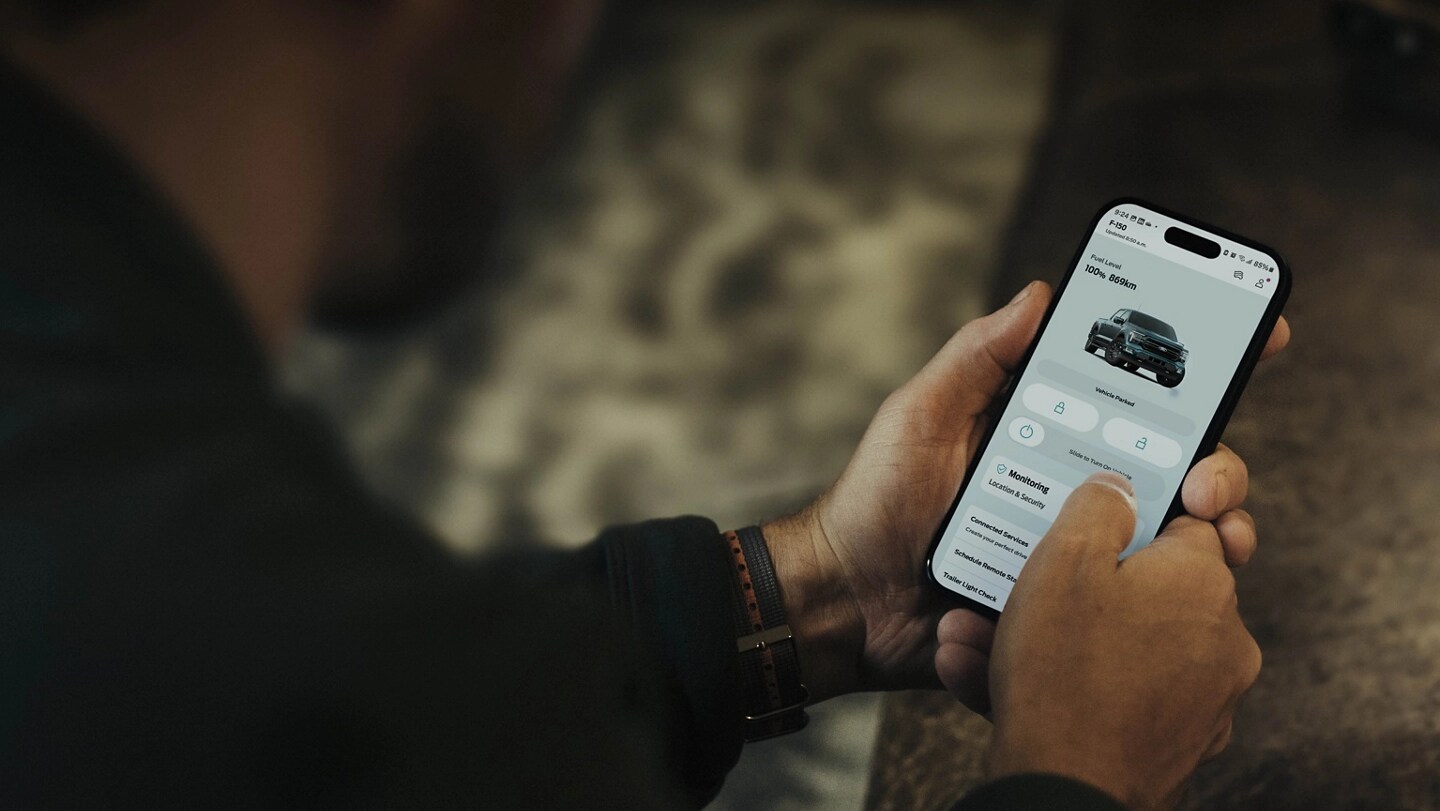 Person holding a smartphone displaying a screen in the Ford app.