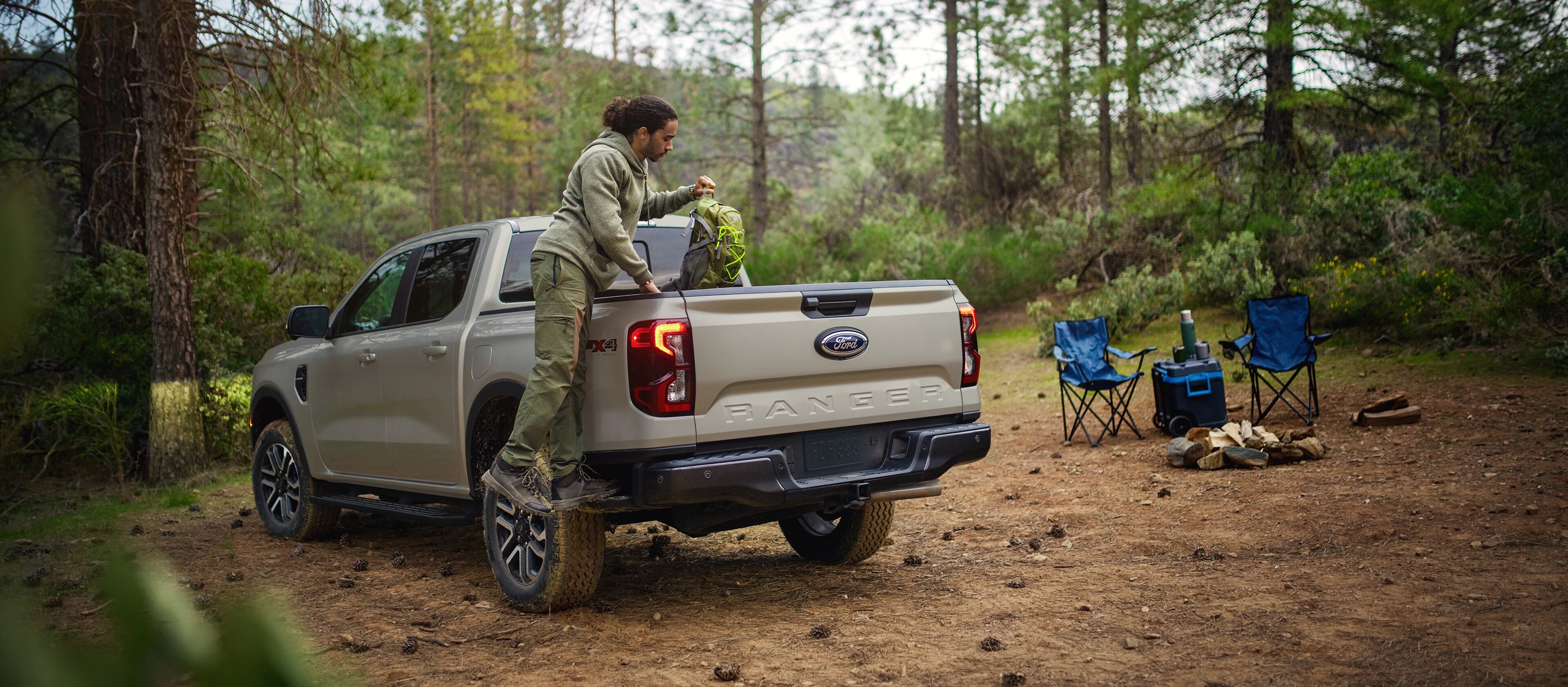 A man is stepping on the side step to put gear into the bed of a 2025 Ford Ranger®