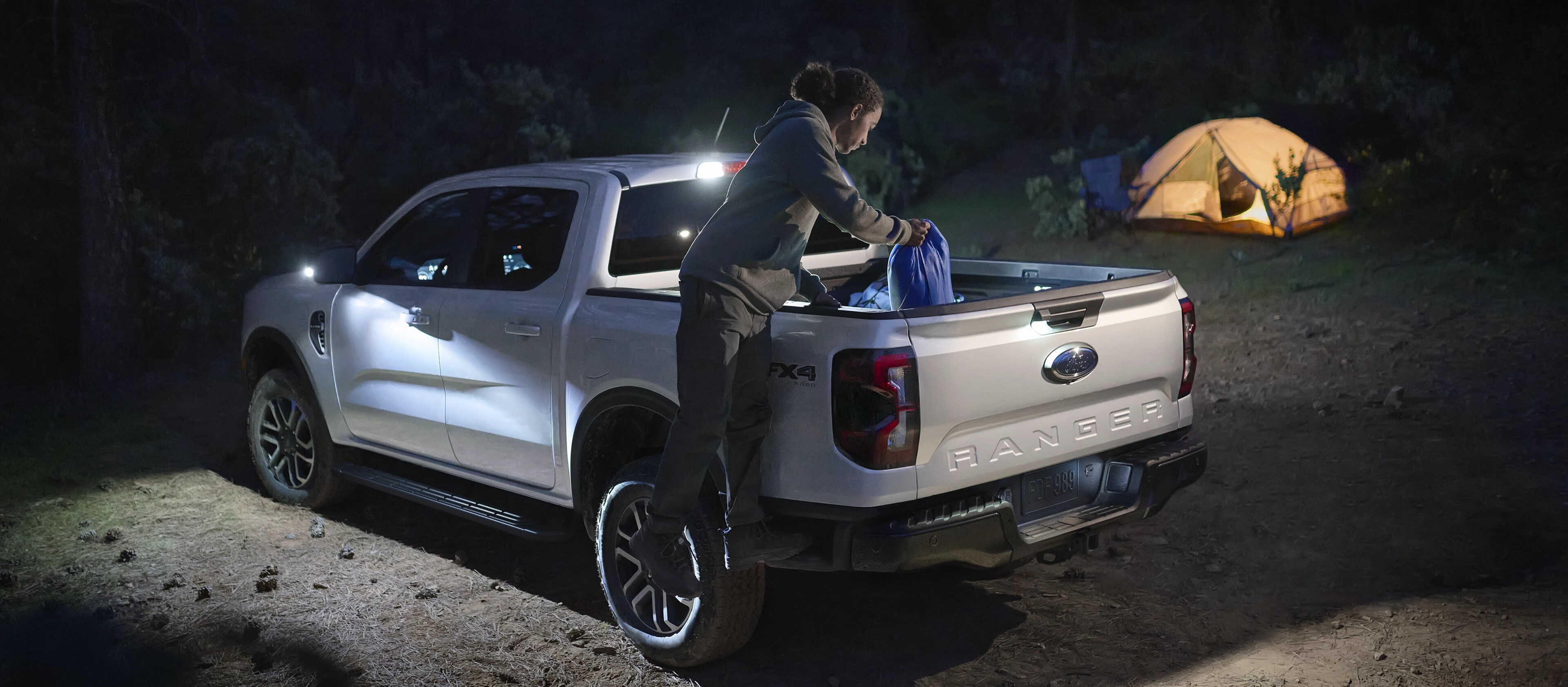 Exterior night shot showcasing the Zone Lighting as a person is getting gear out of the tailgate of a 2025 Ford Ranger®