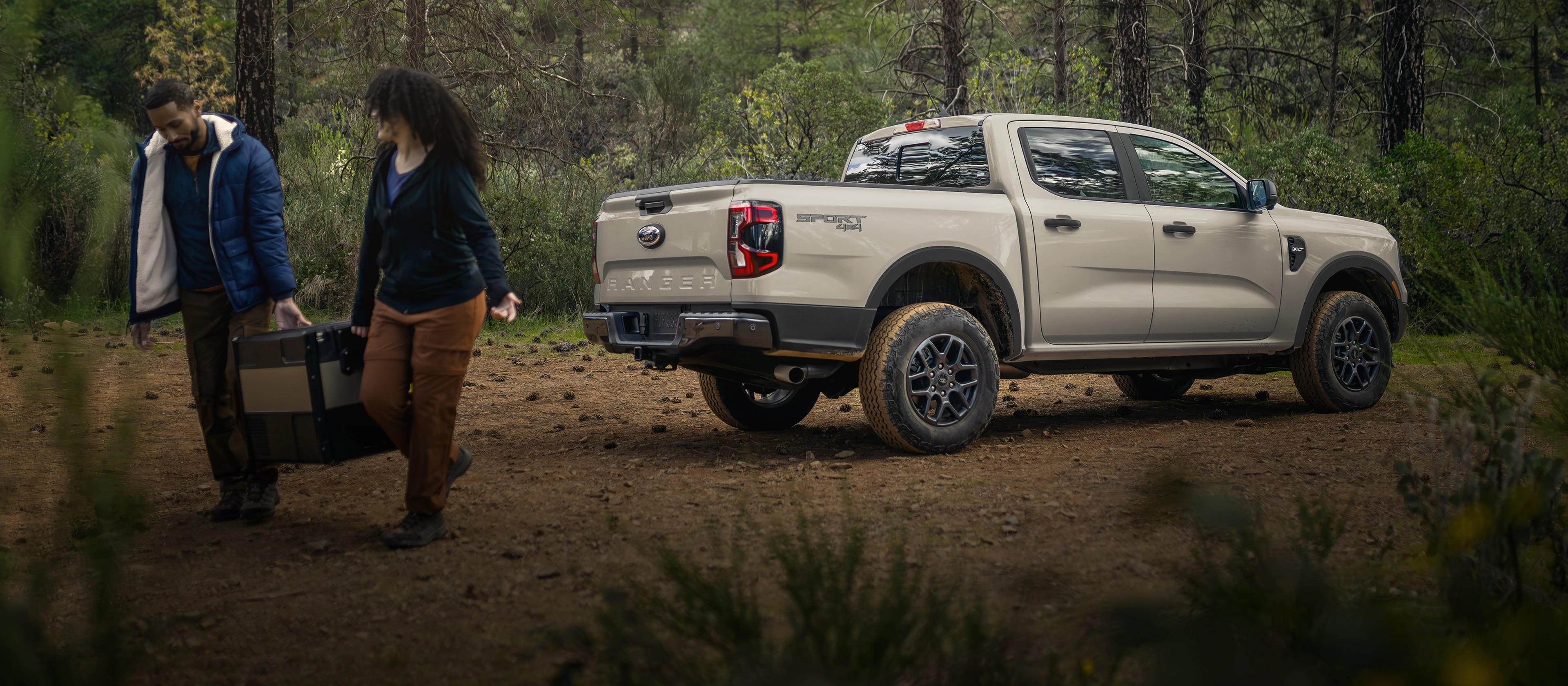 A 2025 Ford Ranger® parked in the woods with a couple walking away from it carrying luggage