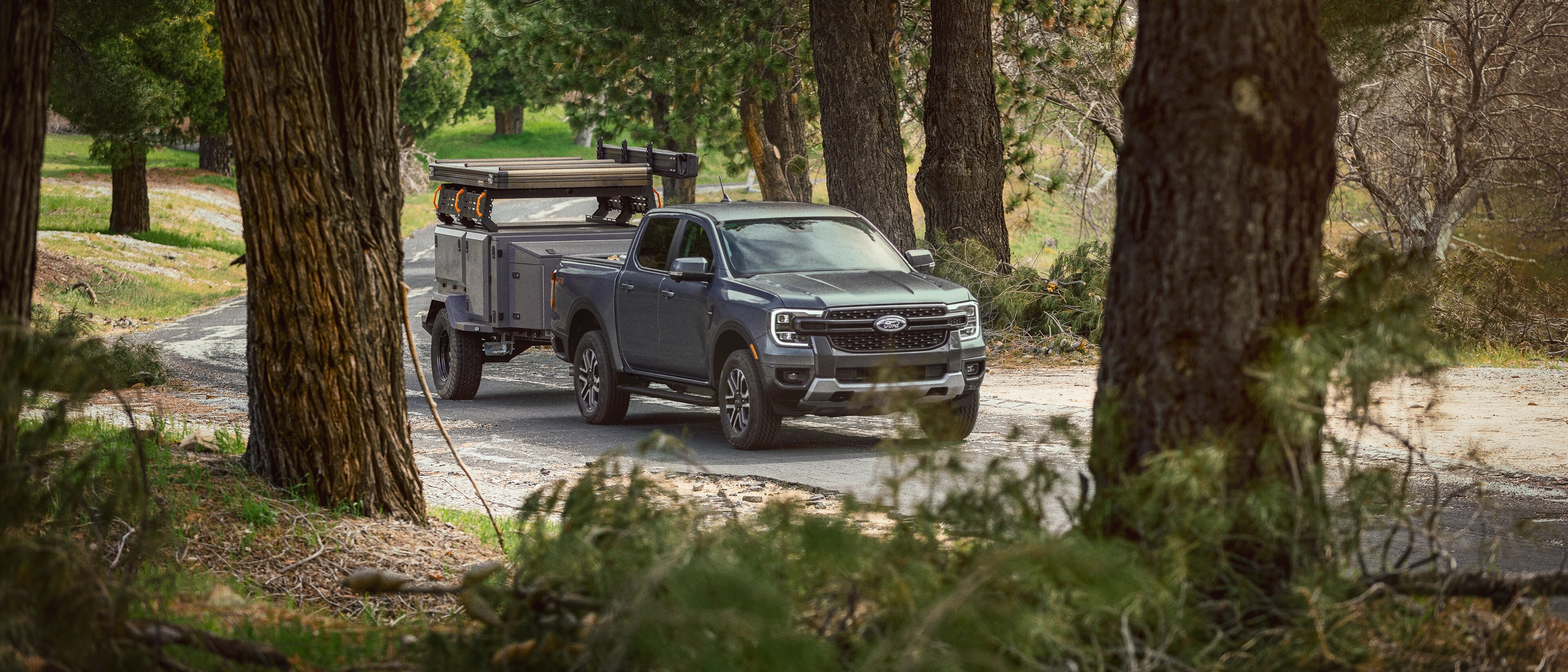 A carbonized grey 2025 Ford Ranger® towing a trailer on a wooded road
