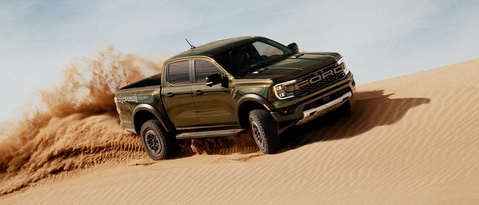 A 2025 Ranger® Raptor® being driven over a sand dune, kicking up sand