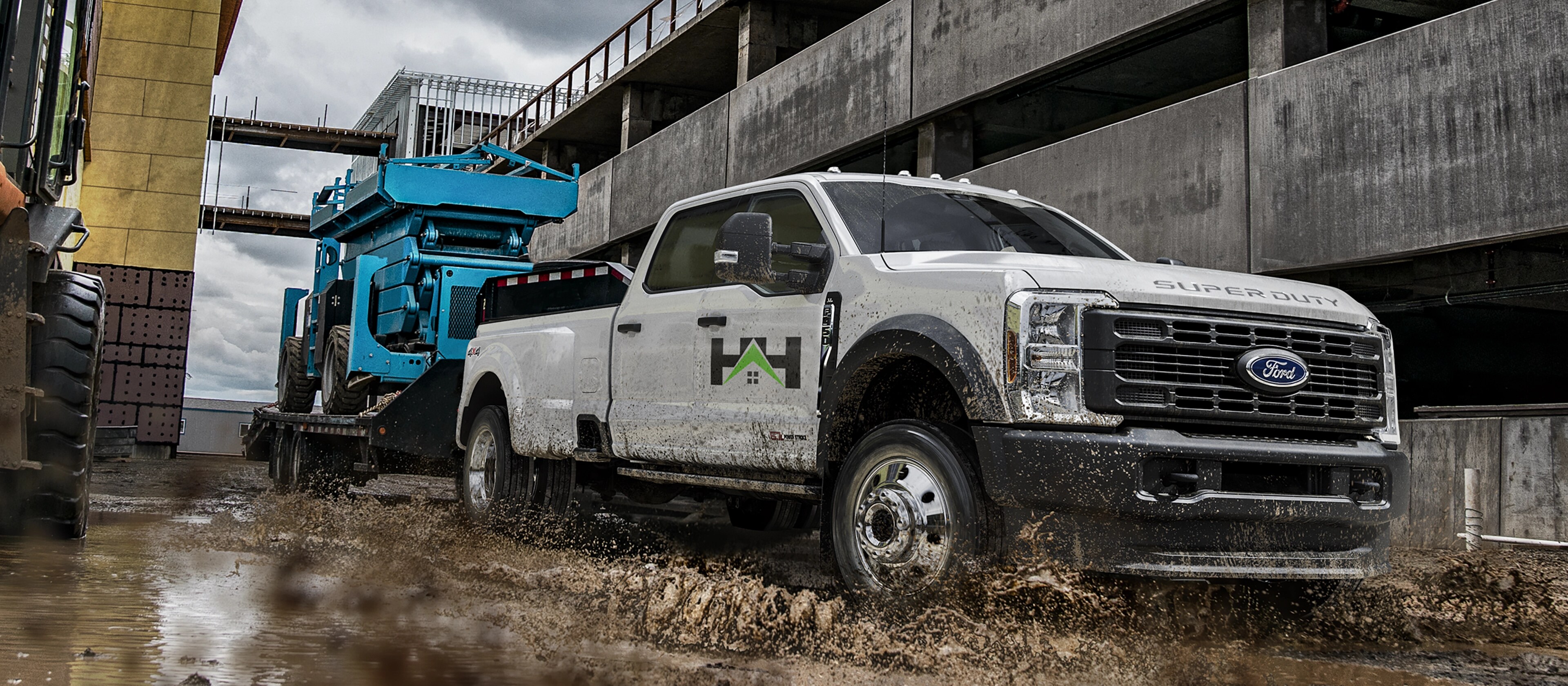 2026 Ford Super Duty® F-450® XL model pulling a flatbed trailer with a large blue tractor on it through mud and water