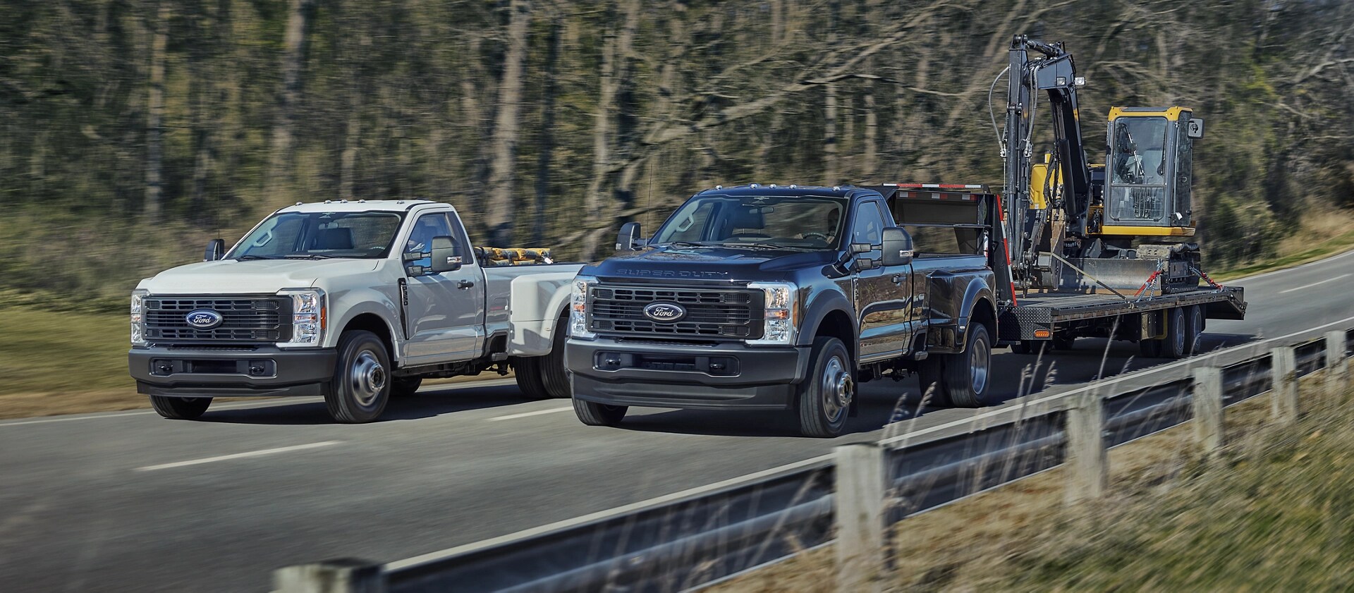 Two 2026 Ford Super Duty® trucks, one with equipment in the bed and the other pulling a large trailer on a paved road
