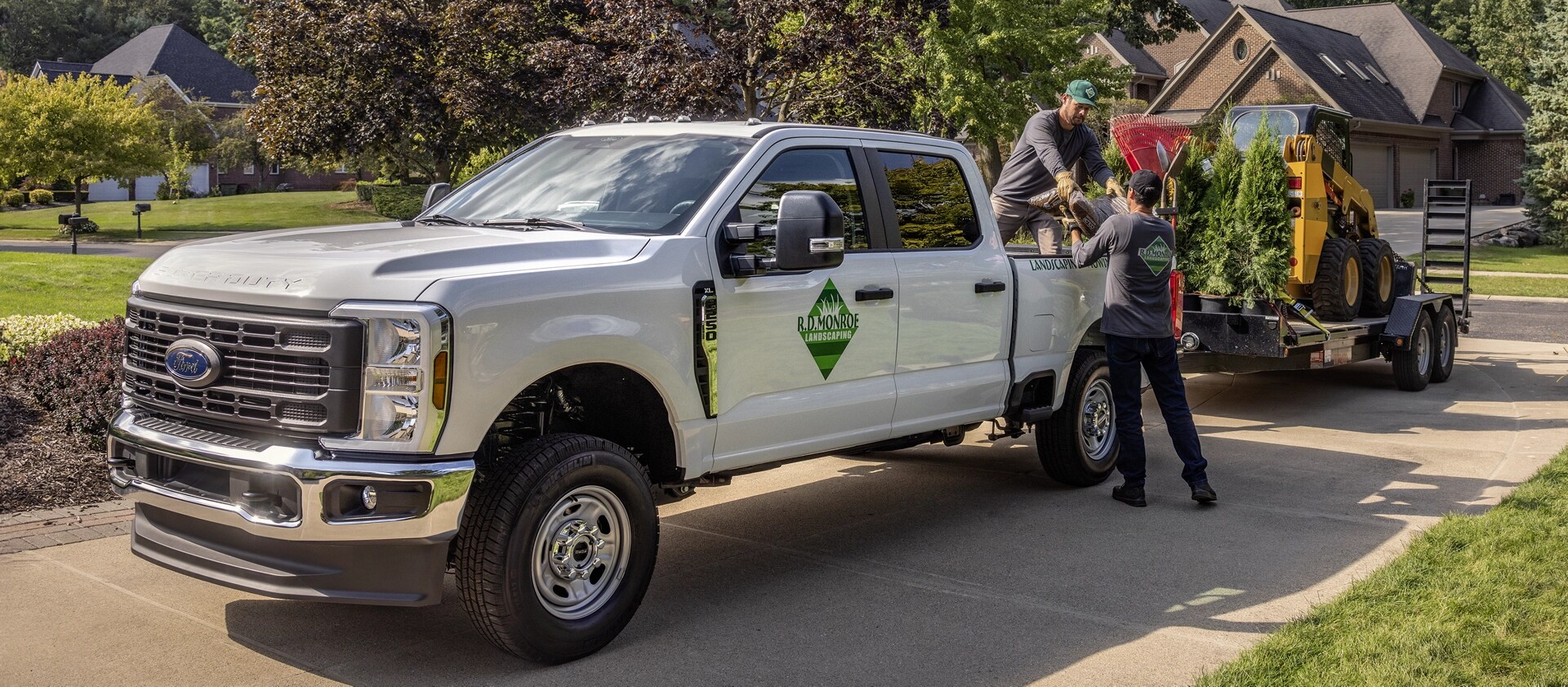 2026 Ford Super Duty® truck parked in a driveway towing a large trailer with equipment for landscaping