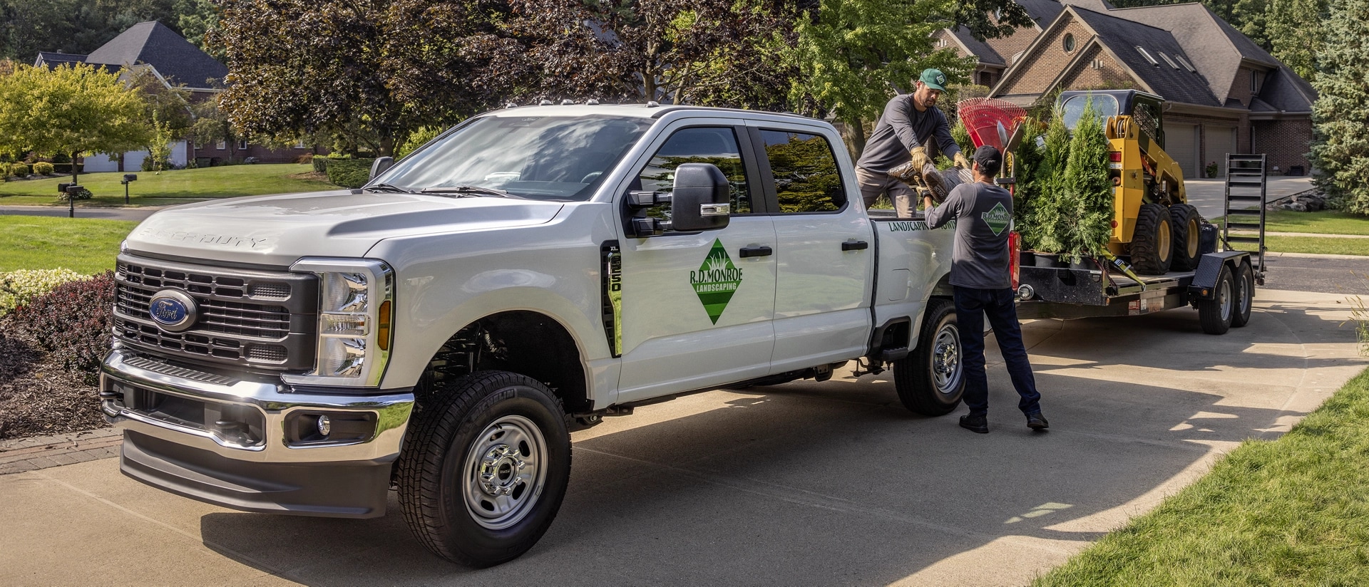 2026 Super Duty® truck parked in a driveway hitched to a trailer carrying landscaping equipment