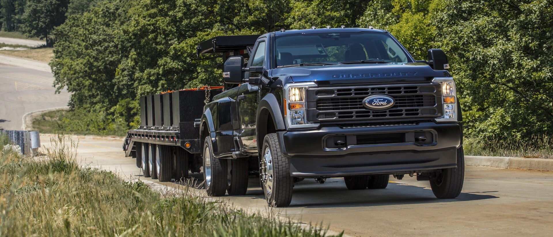 2026 Ford Super Duty® F-350® Platinum® Plus model in Argon Blue pulling a large flat bed trailer up a paved hill