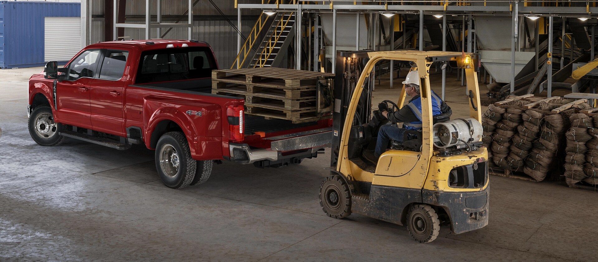 2026 Ford Super Duty® F-350® Lariat® model with the tailgate open while a forklift loads wooden palettes into the truck bed