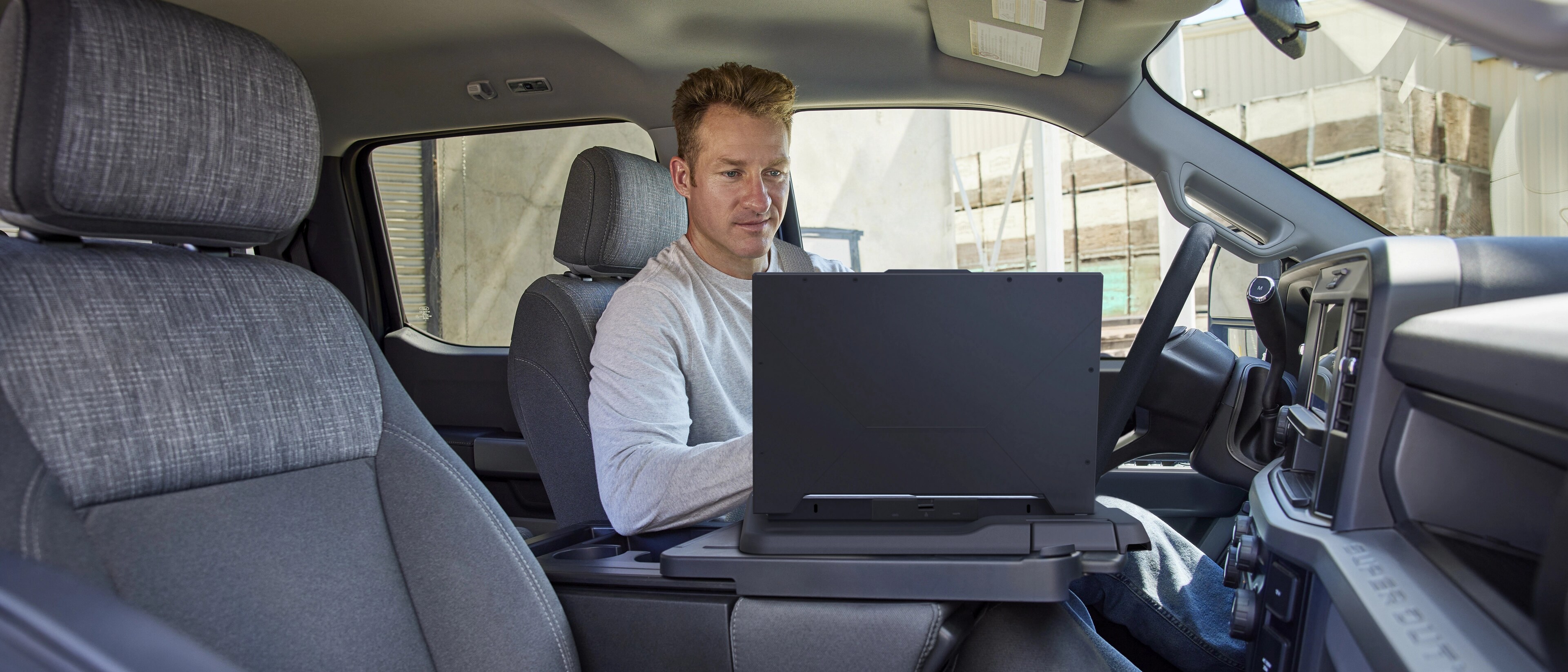 Person working on a laptop using the interior work surface feature inside the cabin of their 2026 Ford Super Duty® truck