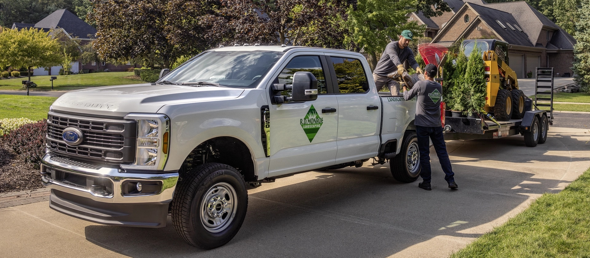 2026 Ford Super Duty® truck parked in a driveway towing a large trailer with equipment for landscaping