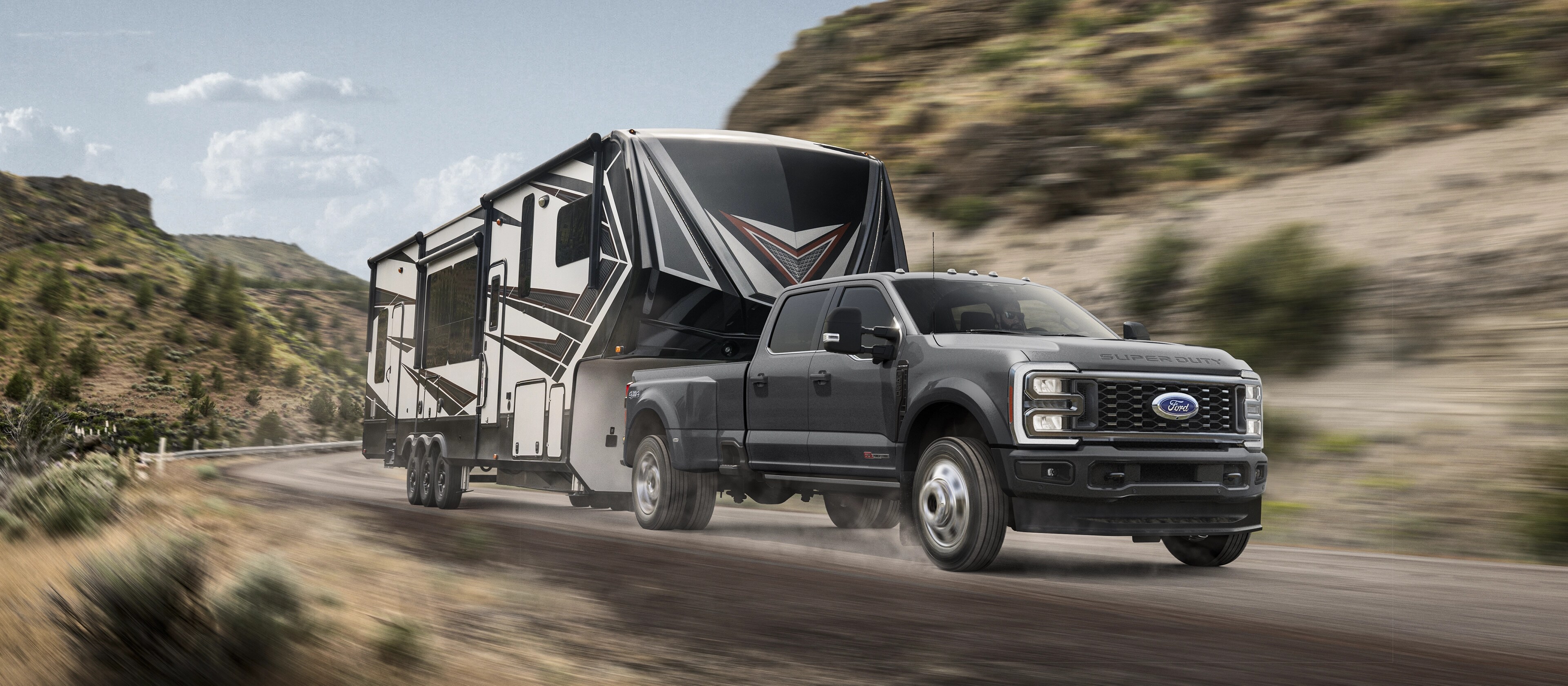 2026 Super Duty® F-450® Platinum® model in Carbonized Grey pulling a camper on a mountain road