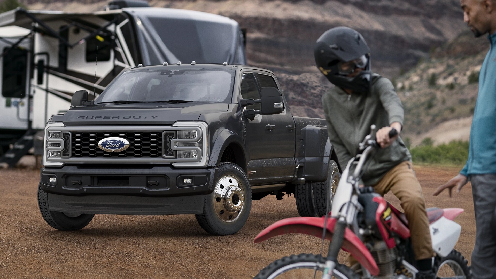 2026 Ford Super Duty® F-450® Platinum® model in Carbonized Grey parked on a campground with campers in the background and a person on a bike in the foreground.