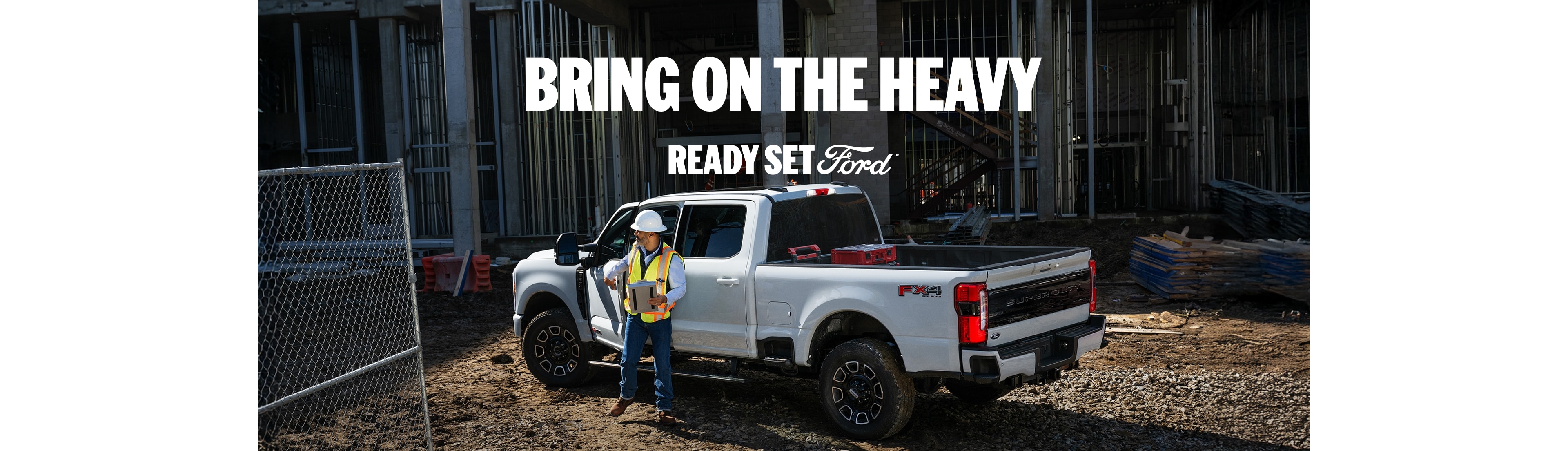 Construction worker stands next to a white Ford Super Duty truck at a construction site