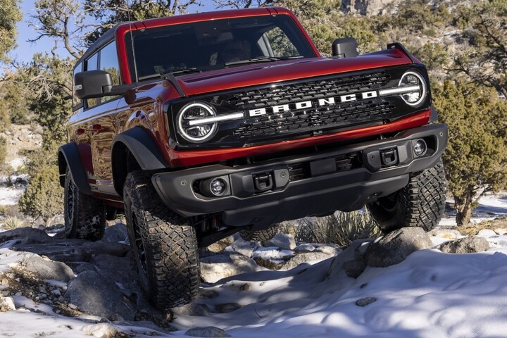 4-door 2023 Ford Bronco® Wildtrak™ model in Race Red off-roading on rough snowy terrain