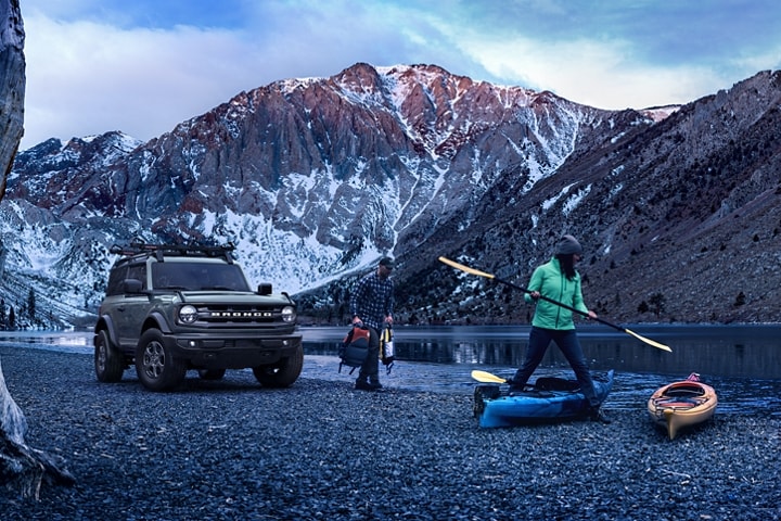 2-door 2023 Ford Bronco® Big Bend™ model in Cactus Grey parked by a mountain lake with people kayaking