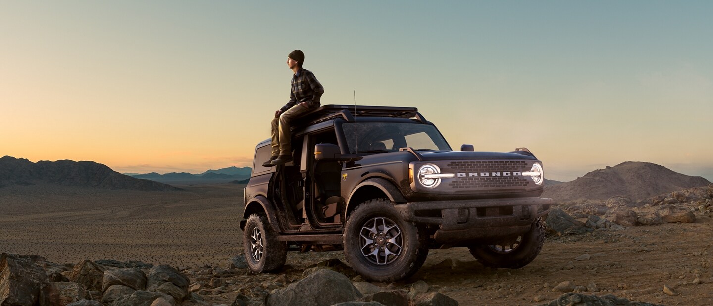 Man sitting on top of his 2023 Ford Bronco® SUV at sunset