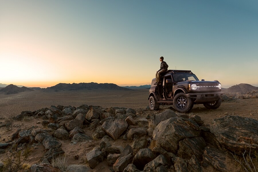Man sitting on top of his 2023 Ford Bronco® SUV at sunset