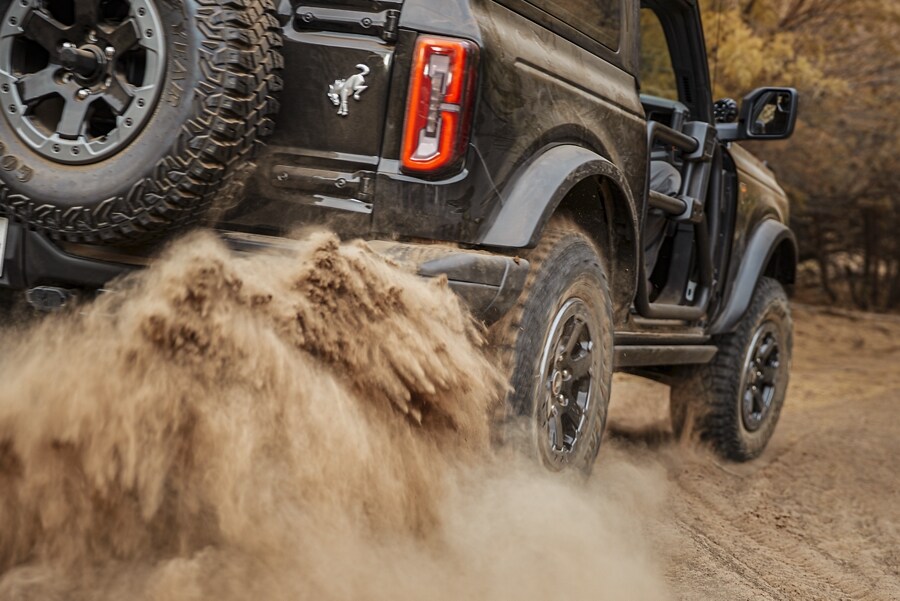 A 2-door 2023 Ford Bronco® Base in Shadow Black being driven down a dirt road