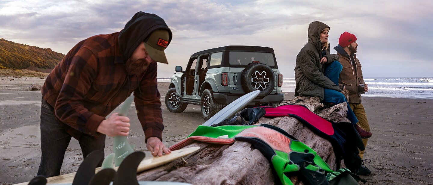 A 2023 Ford Bronco® Outer Banks™ model in Cactus Grey on beach with 3 surfers