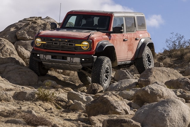 4-door 2023 Ford Bronco® Badlands™ in Hot Pepper Red Metallic Tinted Clearcoat with available modular front bumper being driven on rocks