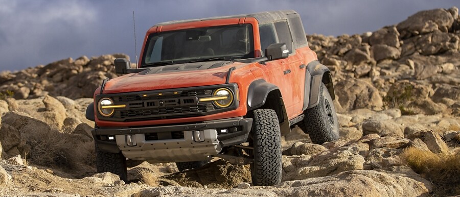 2023 Ford Bronco Raptor® in available Hot Pepper Red Metallic Tinted Clearcoat being driven over huge rocks