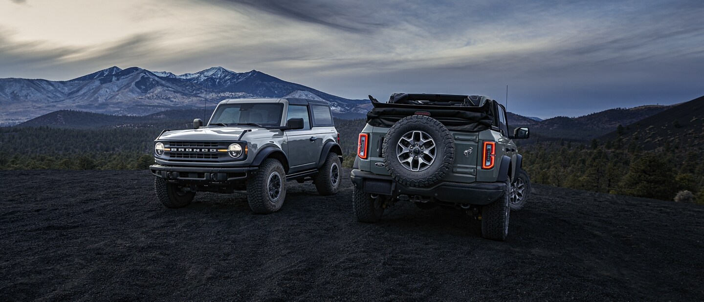 2-door hardtop 2023 Ford Bronco® Black Diamond™ and 4-door 2023 Ford Big Bend™ model soft top parked at dusk in the mountains