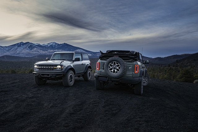 2-door hardtop 2023 Ford Bronco® Black Diamond™ and 4-door 2023 Ford Big Bend™ model soft top parked at dusk in the mountains
