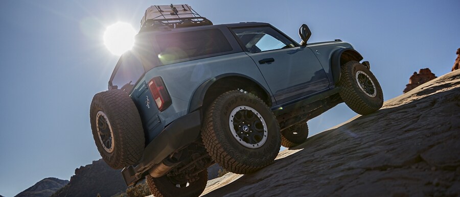 2-door 2023 Ford Bronco® Black Diamond™ in Azure Grey Metallic Tri-Coat being driven up a steep incline