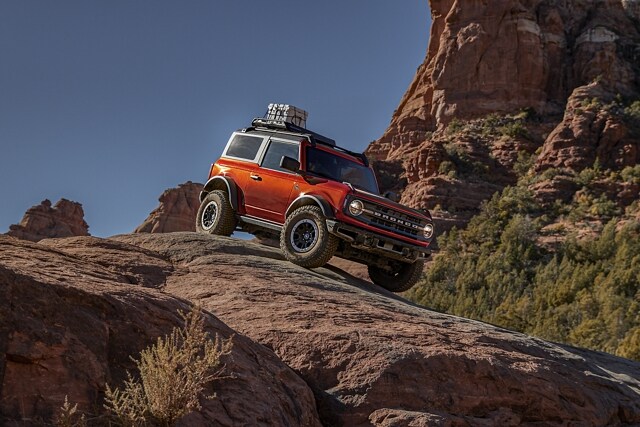 2-door 2023 Ford Bronco® Black Diamond™ in Hot Pepper Red Metallic Tinted Clearcoat being driven down a rocky decline