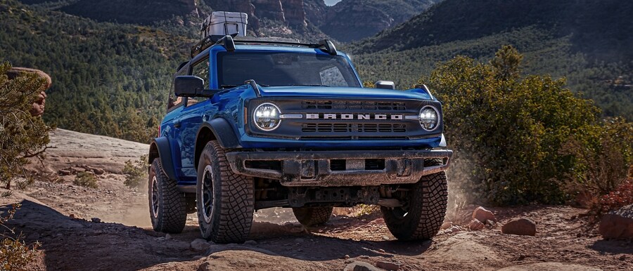 A 2-door 2023 Ford Bronco® Black Diamond™ in Velocity Blue Metallic being driven on a trail