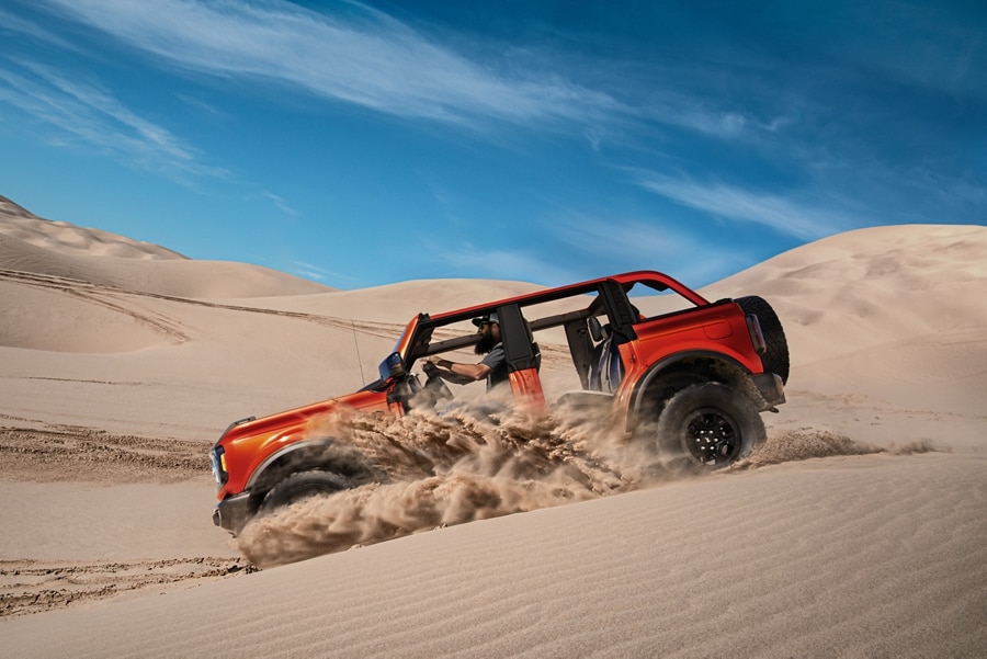 A 2024 Ford Bronco® model in Hot Pepper Red Metallic, an extra-cost paint option, being driven down a sand dune