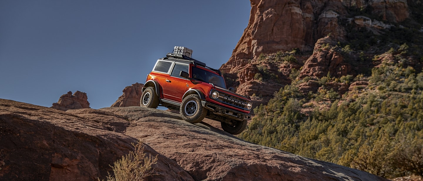 2-door 2024 Ford Bronco® Black Diamond™ in Hot Pepper Red Metallic Tinted Clearcoat being driven down a rocky decline