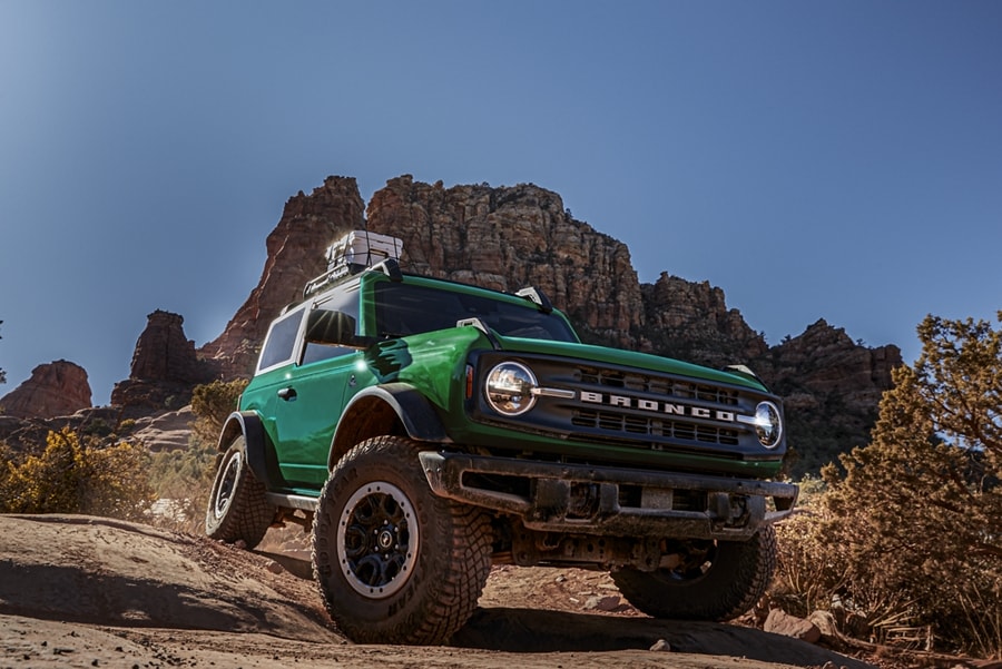 A 2-door 2024 Ford Bronco® Black Diamond™ in Eruption Green Metallic being driven over desert terrain