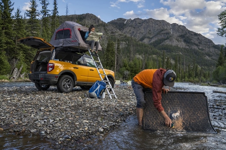 Shown is a man in a river washing off his cargo mat for his 2023 Ford Bronco® Sport SUV