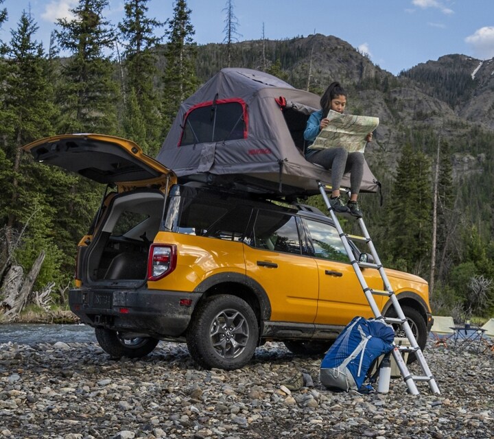 2023 Ford Bronco® Sport SUV shown with liftgate open and a woman sitting in a tent on the roof