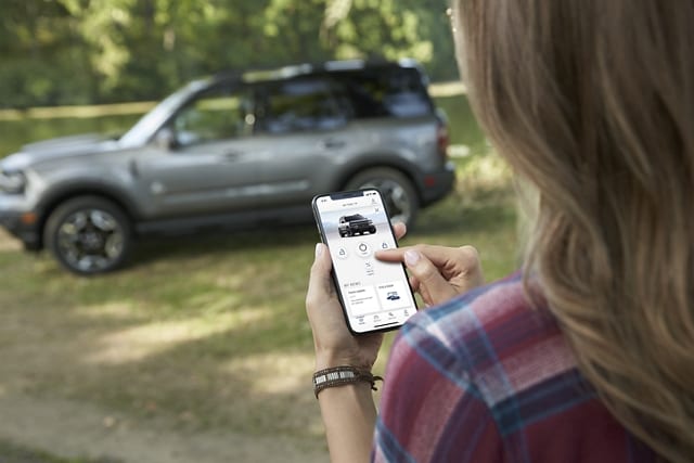 A woman holding a smartphone uses her FordPass™ App to remote start her 2023 Ford Bronco® Sport SUV