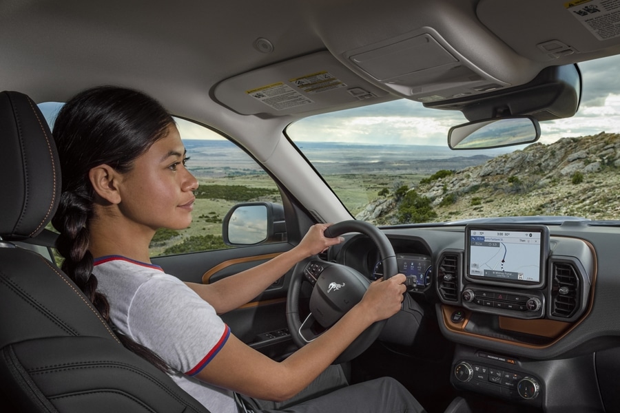 Woman sitting in a 2024 Ford Bronco® Sport SUV with hands on the steering wheel looking at a map on the interior screen