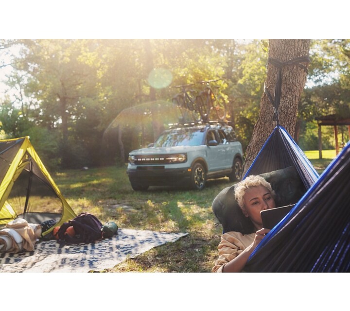 A woman lying in a hammock with gear on a blanket behind her with a 2024 Ford Bronco® Sport SUV is in the background