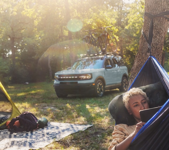 A woman lying in a hammock with gear on a blanket behind her with a 2024 Ford Bronco® Sport SUV is in the background