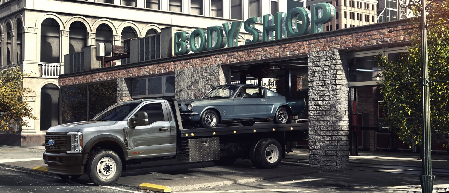 2023 Ford Super Duty® Chassis Cab pulling out of body shop garage with car on back flatbed