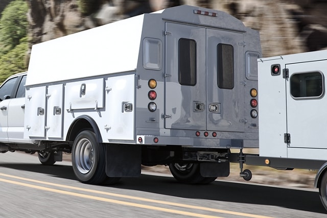 2023 Ford Super Duty® Chassis Cab with utility box upfit and trailer in tow being driven on road near trees